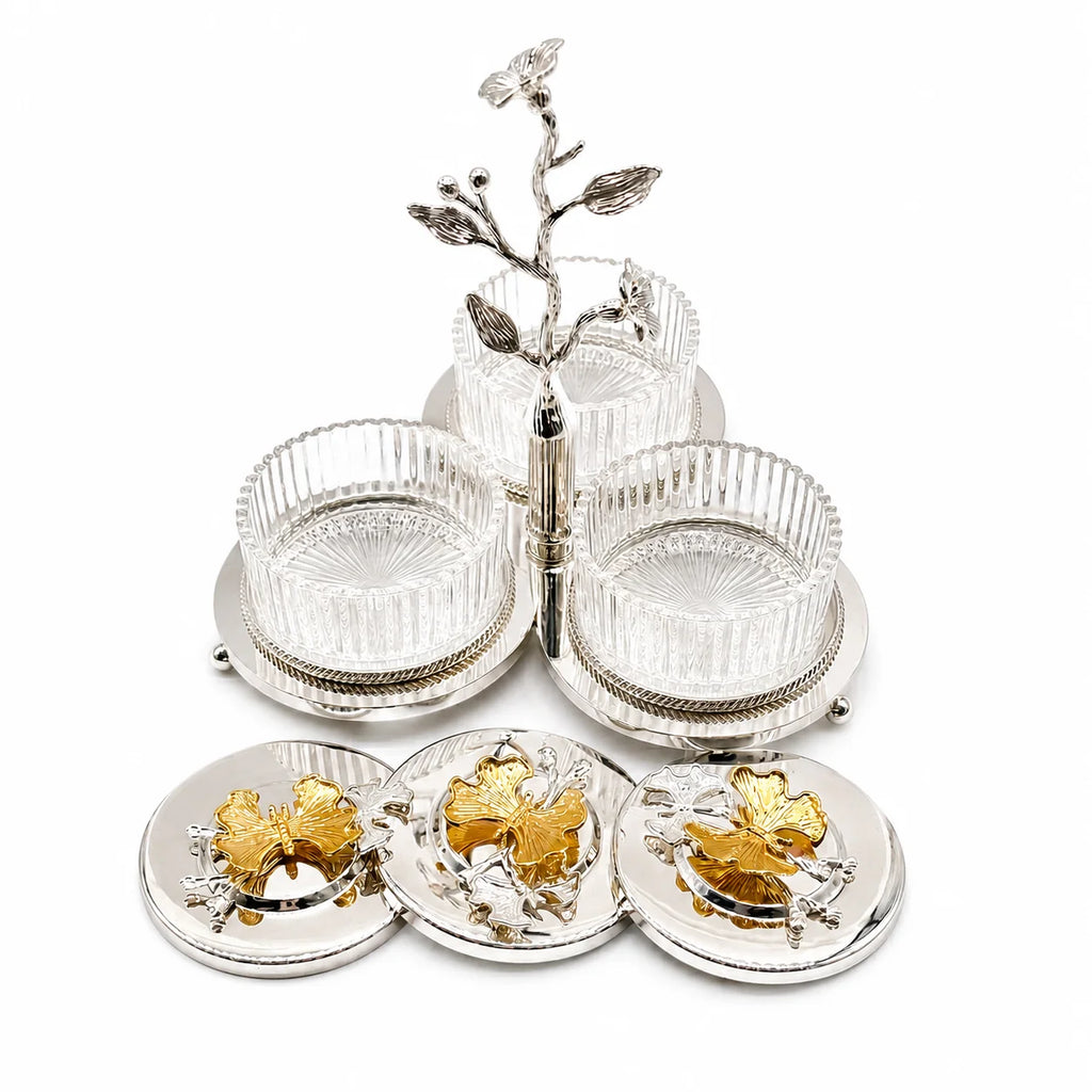 A silver-toned five-bowl salt and pepper grinder set with clear ribbed glass bowls, a decorative silver branch stand, and three round silver lids featuring gold-toned floral designs, shown on a white background.