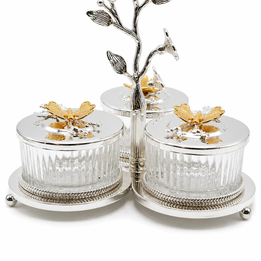Three-piece silver and gold bird-themed caddy set, featuring three ribbed glass jars with silver lids topped with gold bird figurines, mounted on a silver branch stand with small bird perches.
