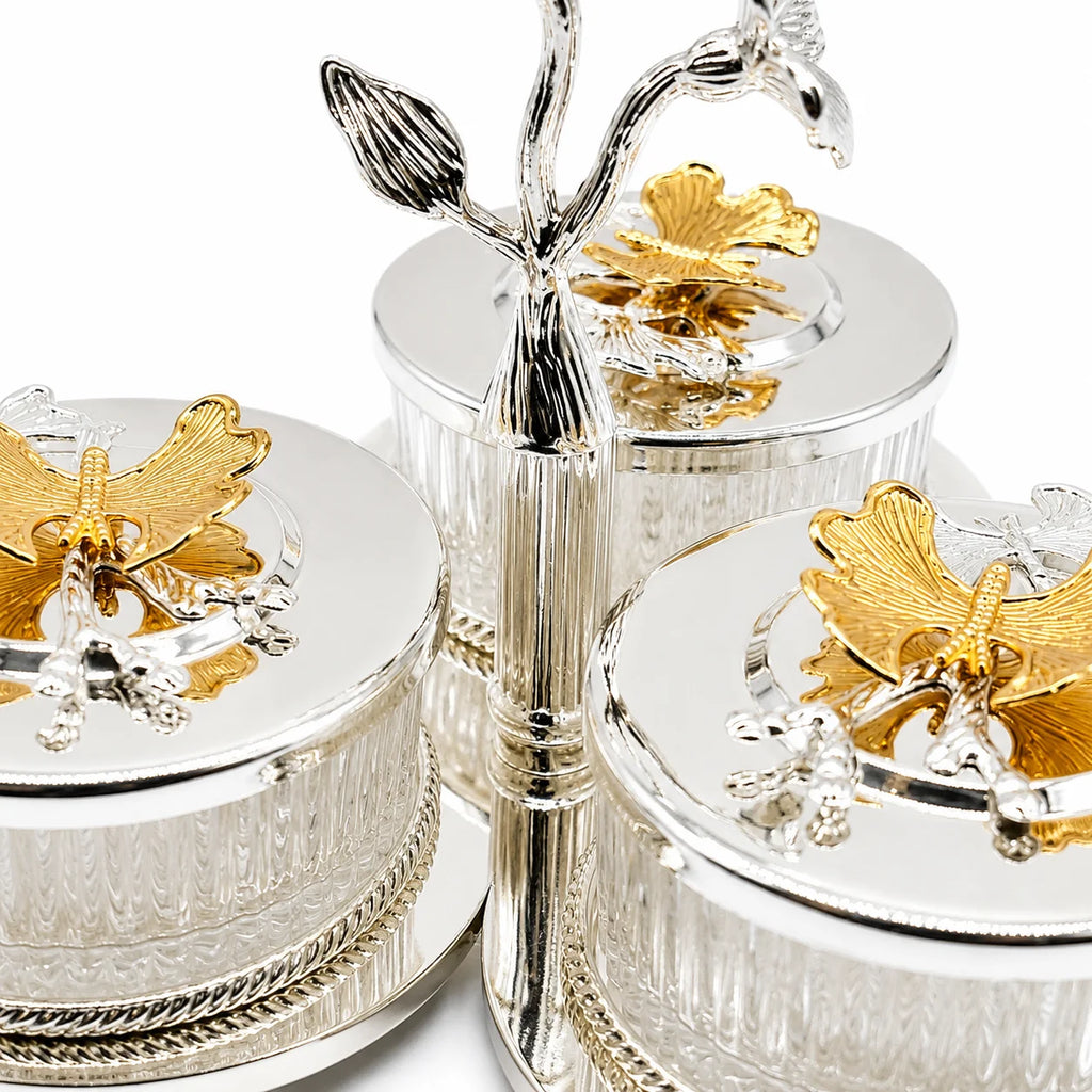 Three round silver-toned glass lidded boxes with gold butterfly and floral lid ornaments, arranged together on a white background.