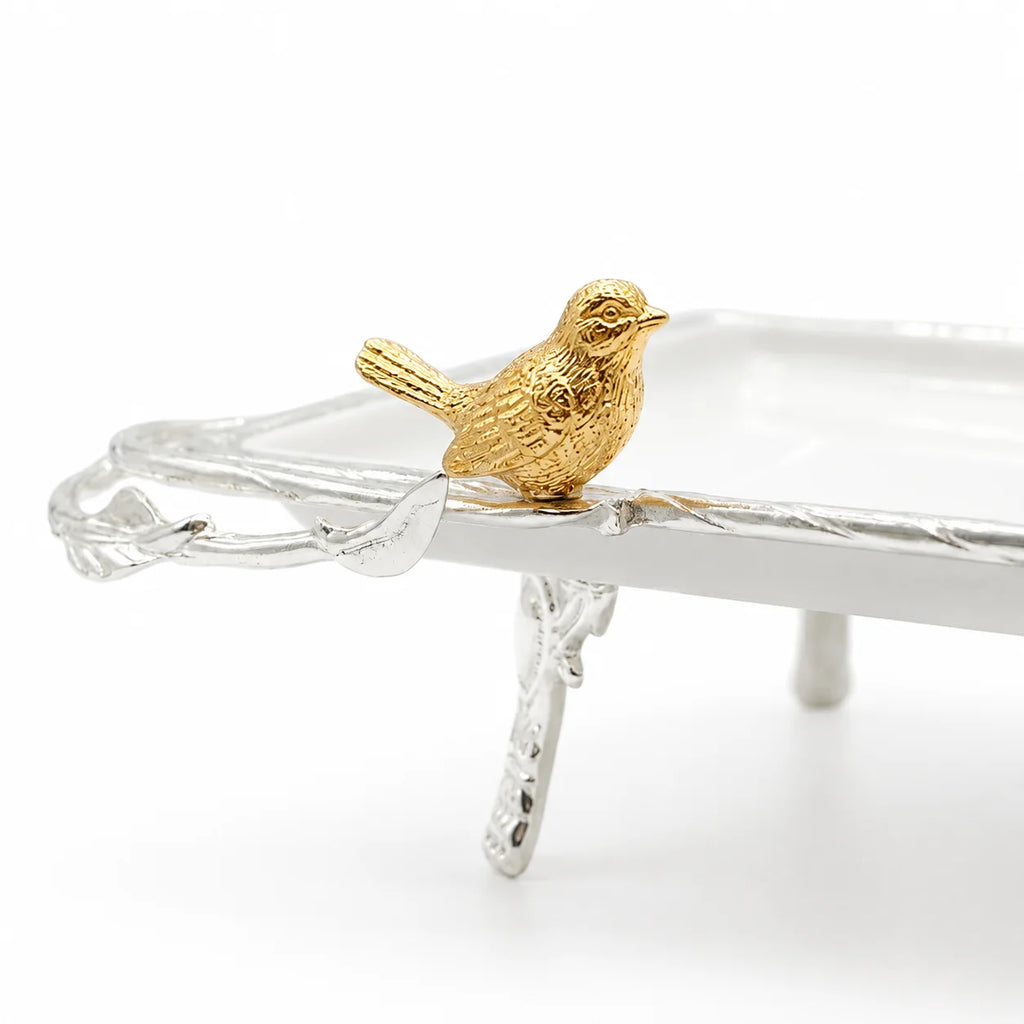 A small textured gold bird figurine perched on the edge of a silver-colored tray, photographed on a clean white background.