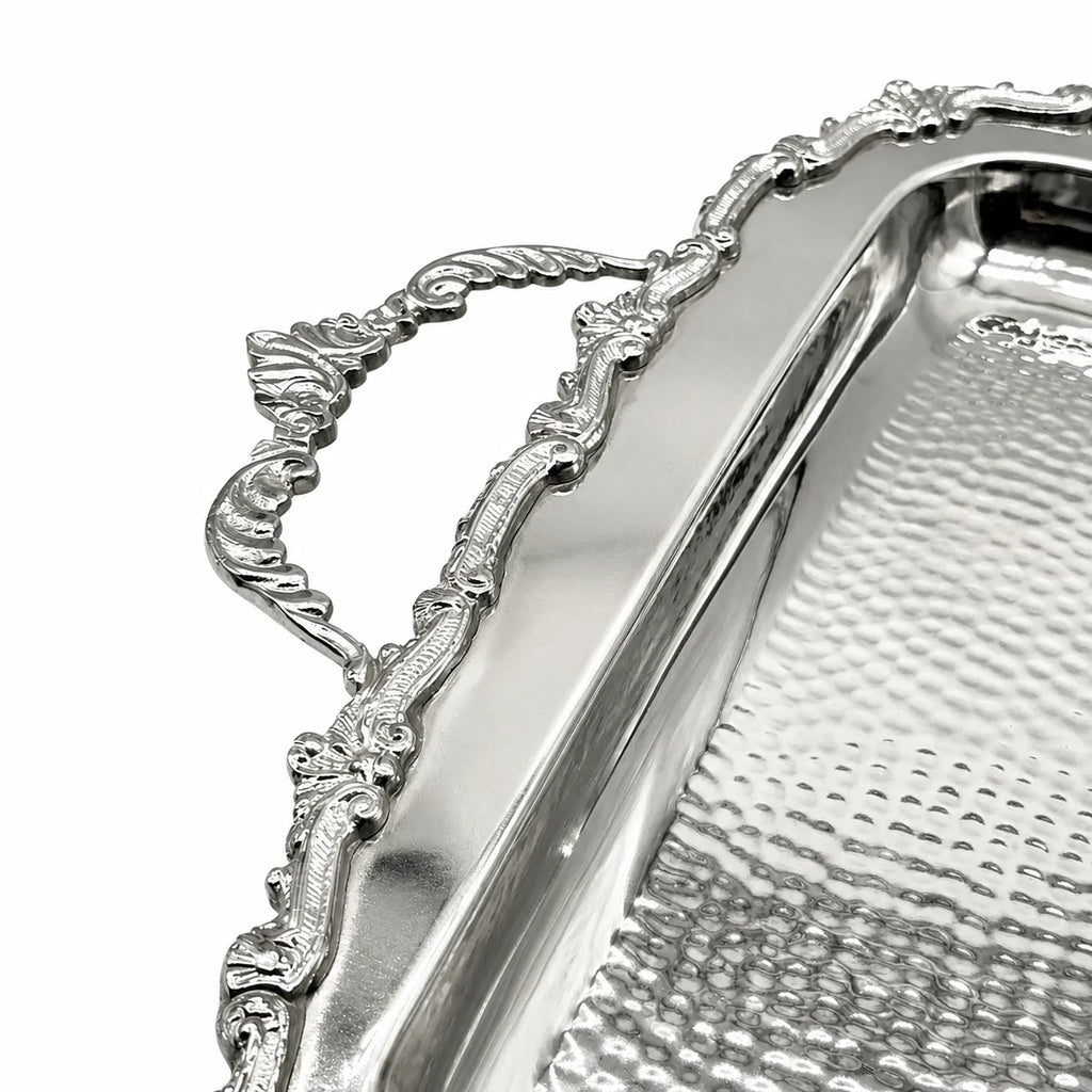 Silver metal serving tray with an ornate decorative handle and hammered textured interior, shown in a close-up studio shot on a white background.